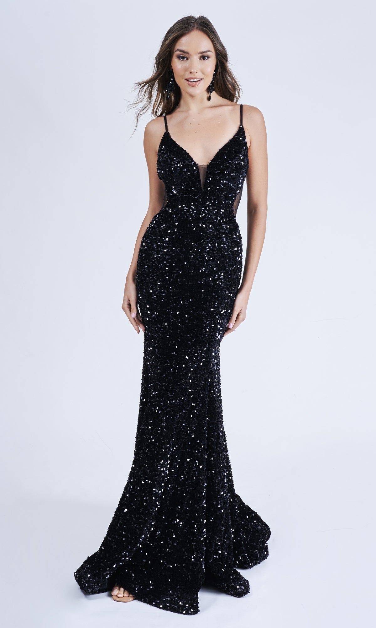 A woman models the Long Formal Sequin Dress: Nina Canacci 4420—a sleeveless, floor-length black gown with a deep sheer v-neckline—standing against a plain light background.